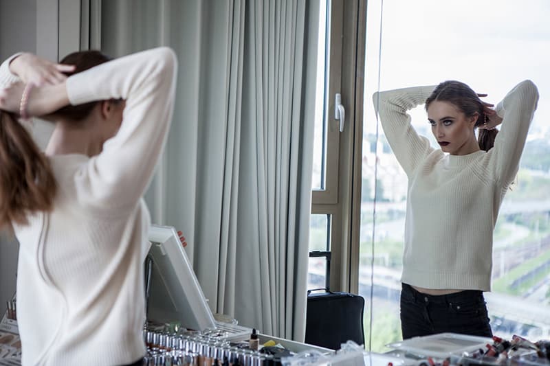 woman in white sweater standing in front of mirror