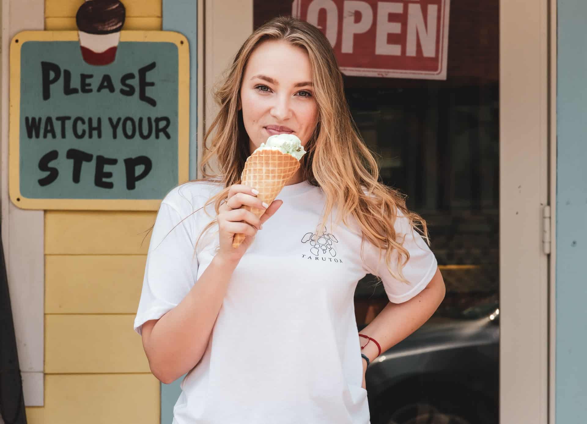 woman in white t-shirt eating ice cream in front of store