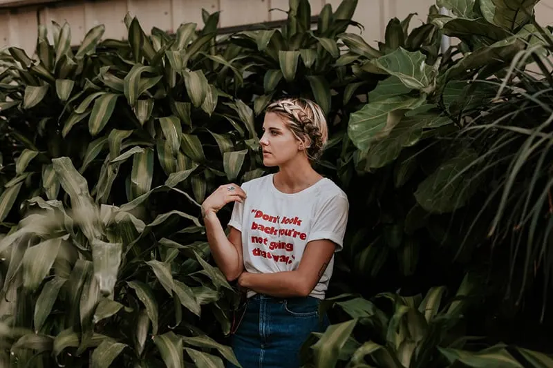 woman in white t-shirt standing near green plants looking aside