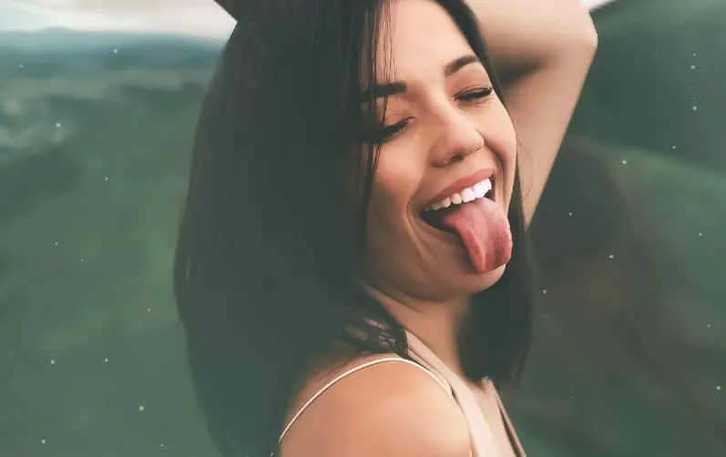 woman in white tank top smiling with mouth opened and tongue out