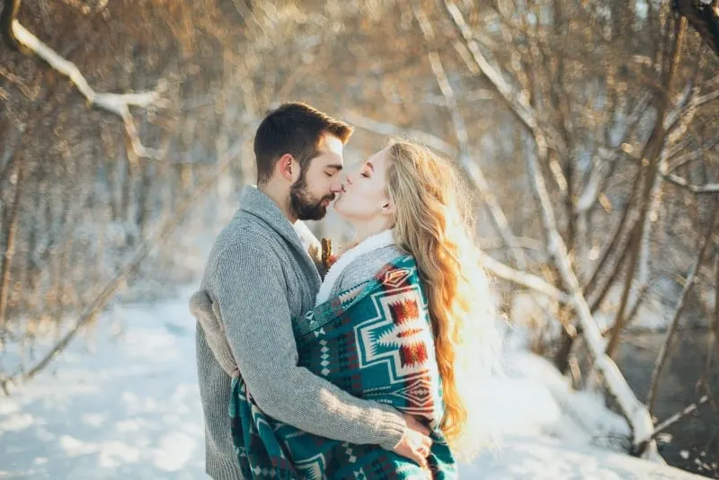 woman wrapped in blanket kissing man's nose in winter