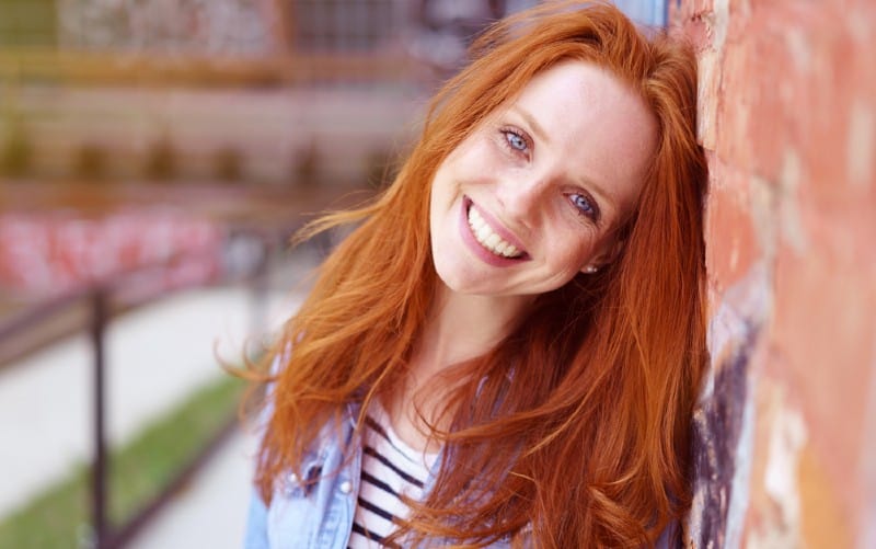Happy red haired woman leaning against a brick wall
