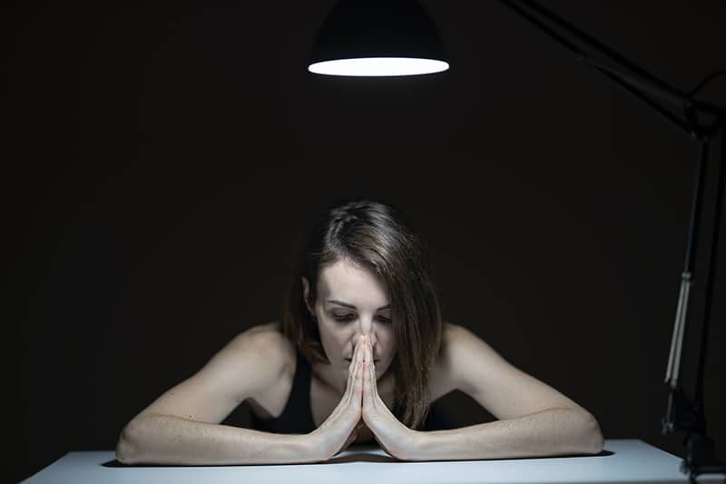 mulher apoiada na mesa com a cabeça debaixo do candeeiro