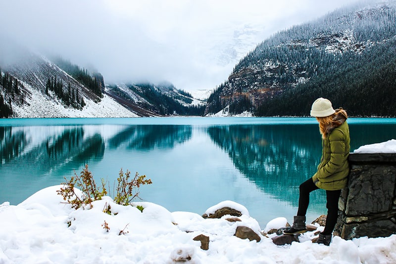 mujer apoyada en la pared cerca del lago en tiempo de nieve