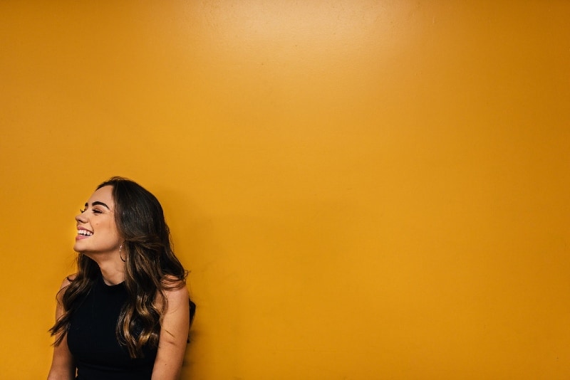 donna in top nero appoggiata a un muro giallo