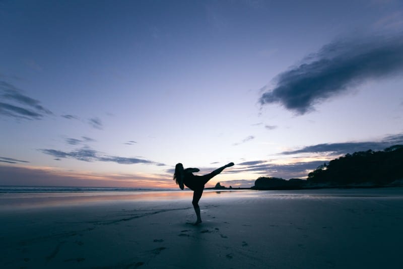 silhouette of woman kicking on mid air on beach