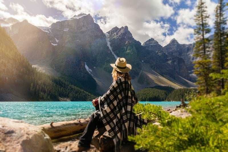 donna con cappello seduta su una roccia che guarda il lago