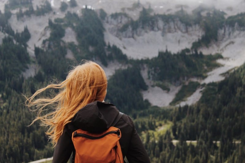 woman with orange backpack looking at mountains during daytime