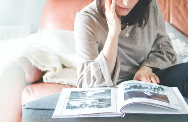 donna che guarda l'album fotografico sul tavolo con il viso appoggiato a una mano