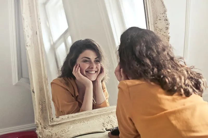 woman looking at the mirror while she is smiling