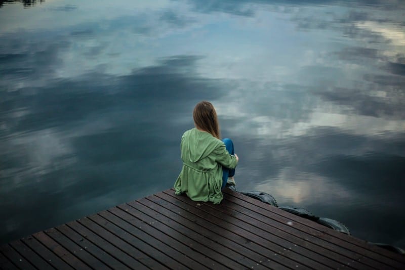 mujer sentada en tablas de madera y mirando el agua