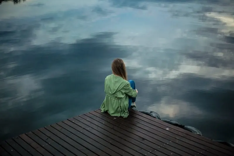 woman sitting on wooden planks and looking at water