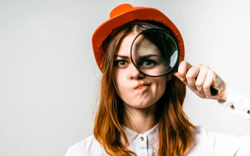 Funny young woman wearing orange hat looking into a magnifying glass