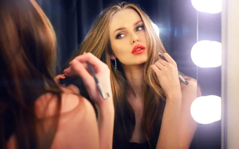 Beautiful woman wearing makeup looking into a mirror