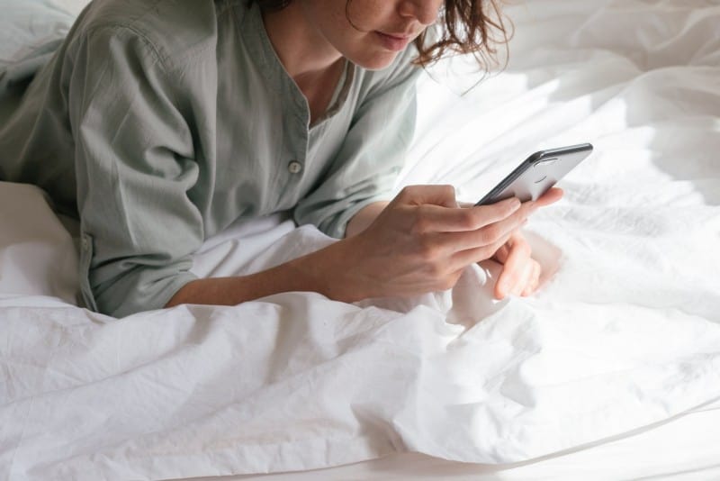 woman lying on bed looking at phone