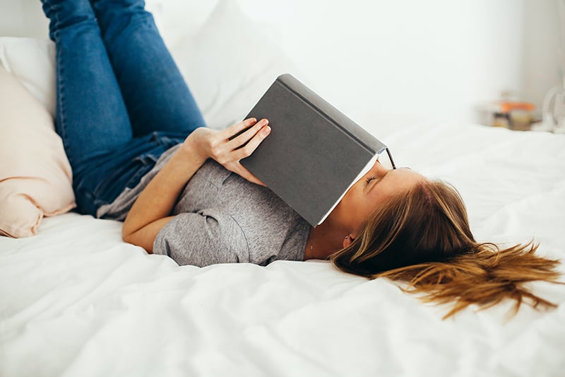 woman lying on bed while covering face with the book