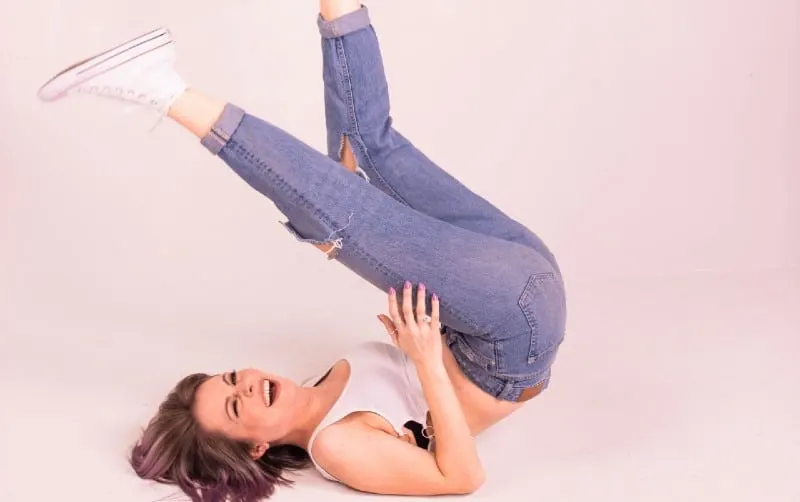 Happy woman wearing blue jeans an dwhite top lying on ground with her legs up