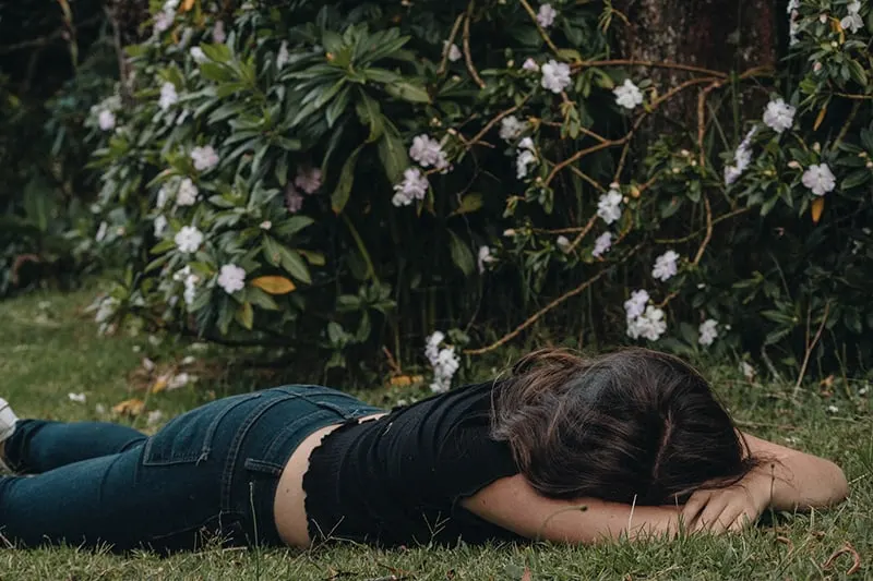 woman lying on the grass near flower bush