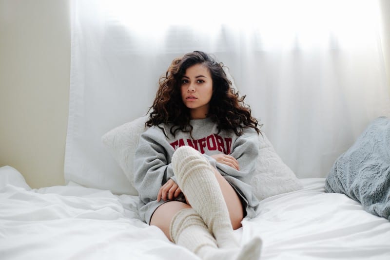 woman in sweatshirt and socks lying on bed