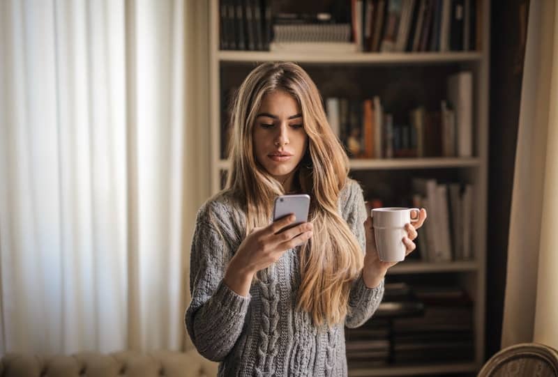 woman on cellphone and mug on the other hand wearing gray sweater