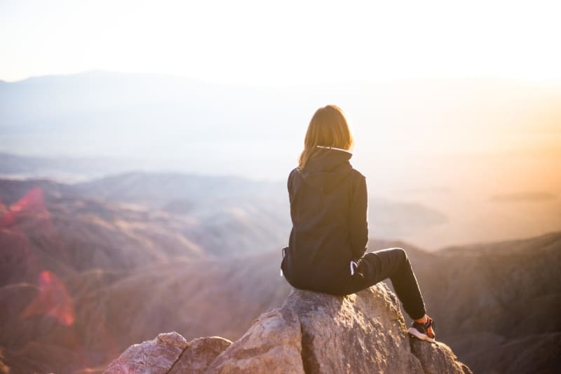 donna seduta in cima alla roccia grigia con vista sulla montagna
