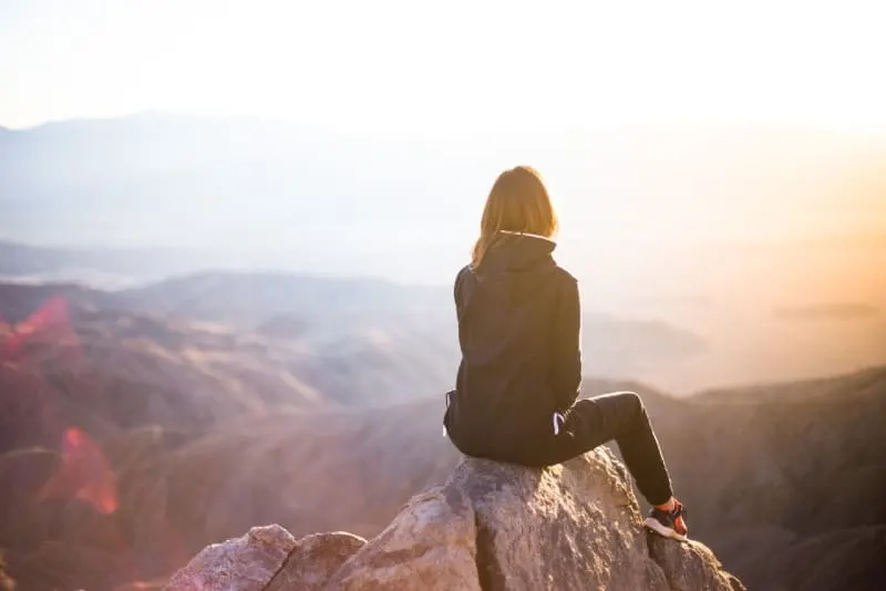 woman sitting on top of gray rock overlooking mountain