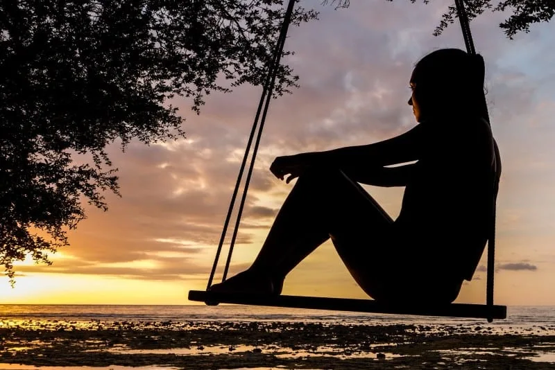 silhouette of woman sitting on swing during golden hour