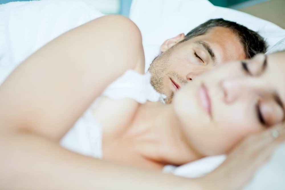woman on white tank top lying in bed with a man