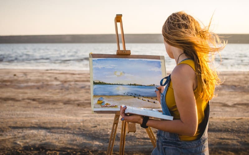 woman painting on the beach near the sea