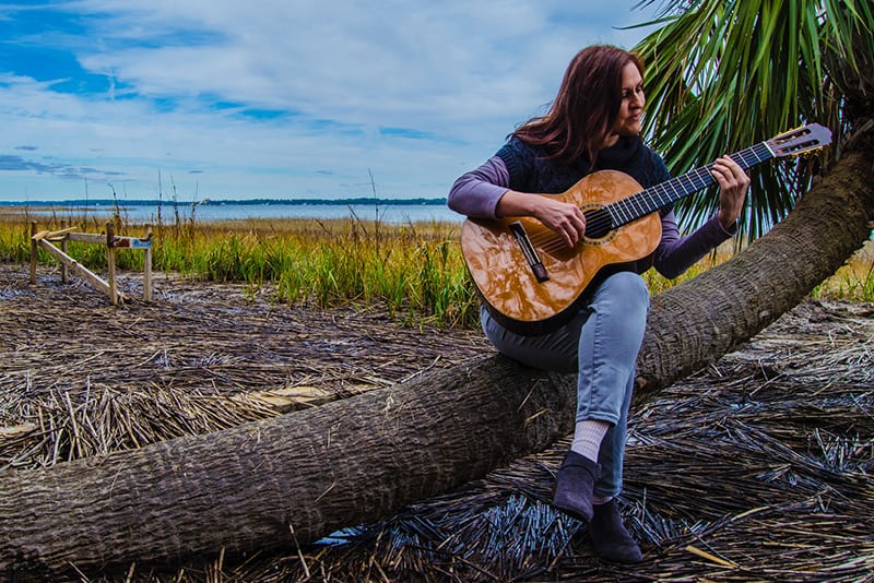 uomo che suona la chitarra classica seduto su un albero di cocco