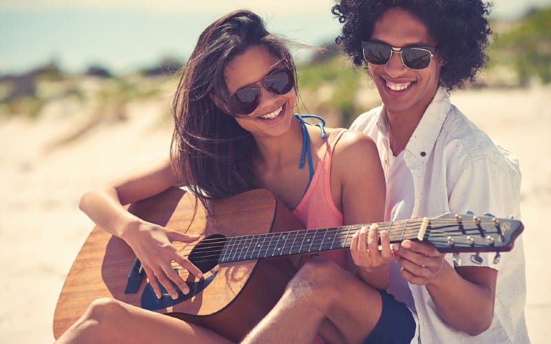 Happy woman playing guitar near man outdoors during daytime