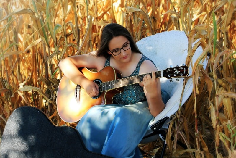 donna che suona la chitarra seduta su una sedia bianca in un campo di grano