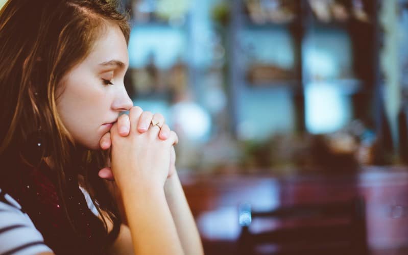 close up of woman praying with closed eyes in blurry background