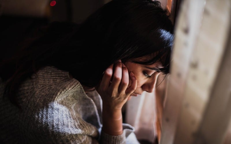 Mujer triste mirando hacia abajo sentada junto a la ventana