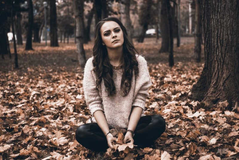 donna in maglione con foglie in mano e seduta a terra