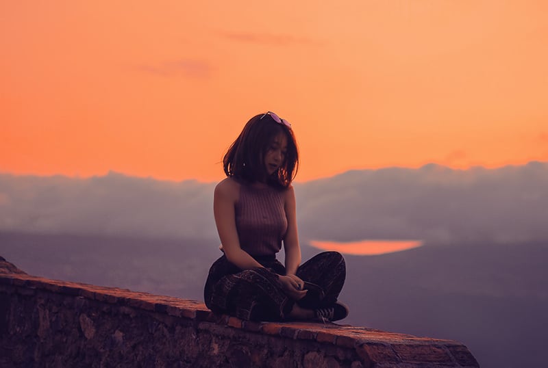 mulher sentada numa falésia durante o pôr do sol