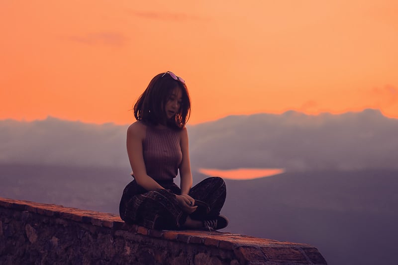 woman sitting on a cliff during sunset