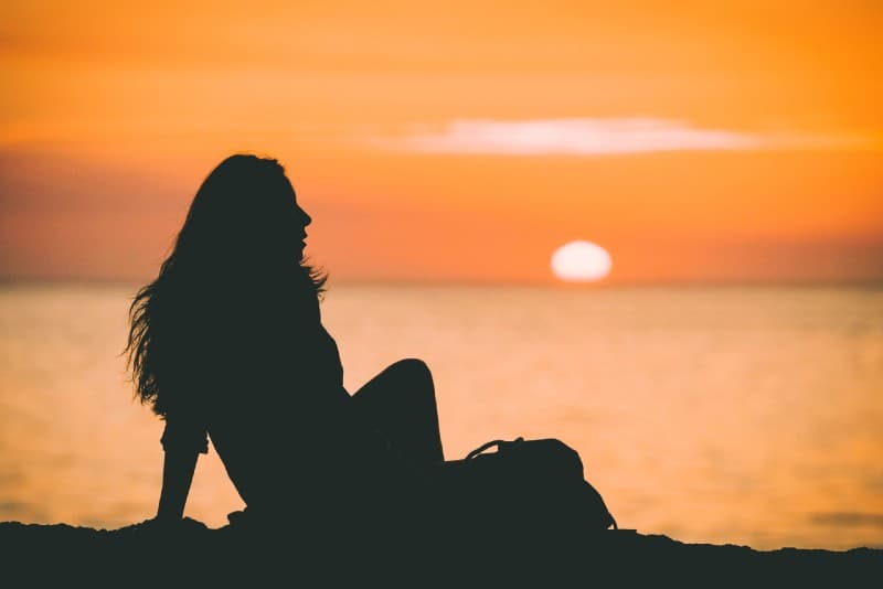 donna seduta sulla spiaggia vicino all'acqua al tramonto