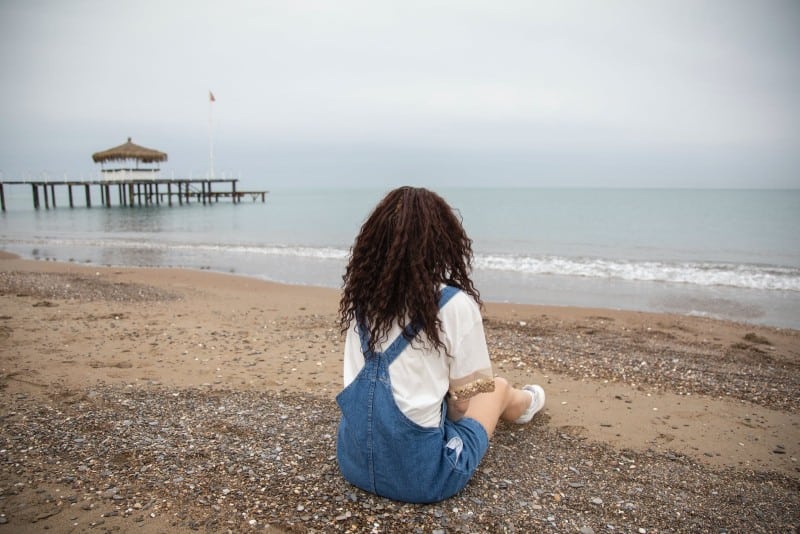 donna seduta sulla spiaggia che guarda il mare