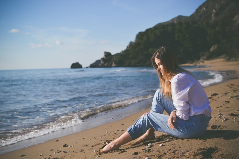 mujer con camisa blanca sentada en la playa