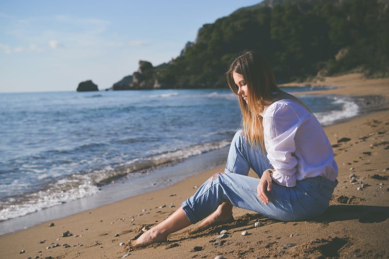 mujer sentada en la orilla de la playa durante el día