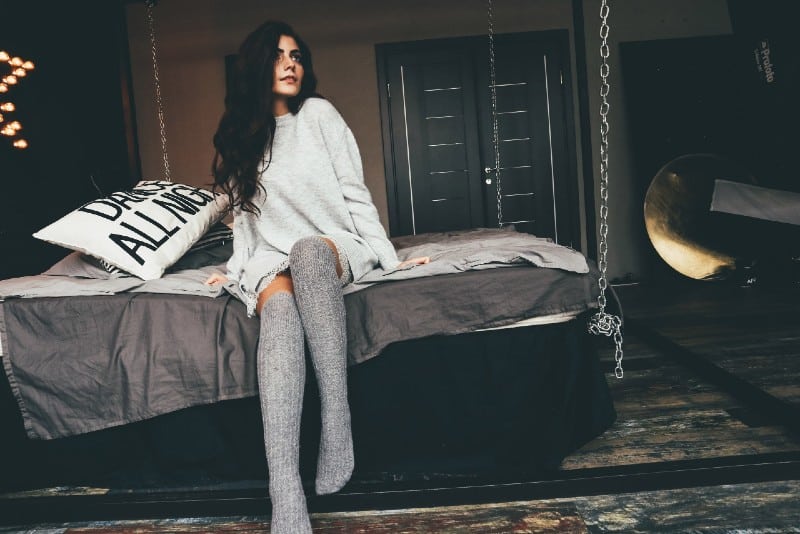 woman with grey sweatshirt and socks sitting on bed