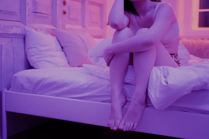 woman sitting on bed with purple lights on not showing the face
