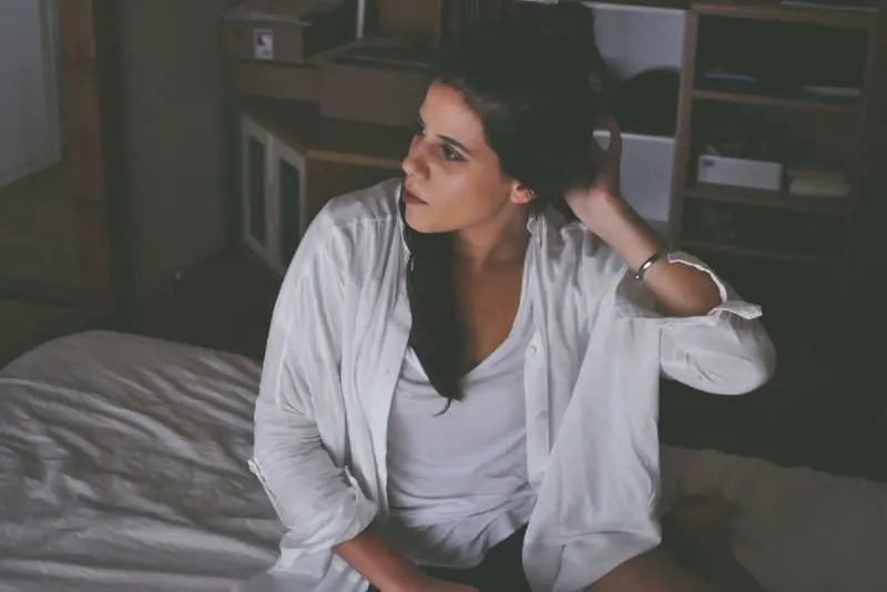 woman in white shirt sitting on bed touching her hair