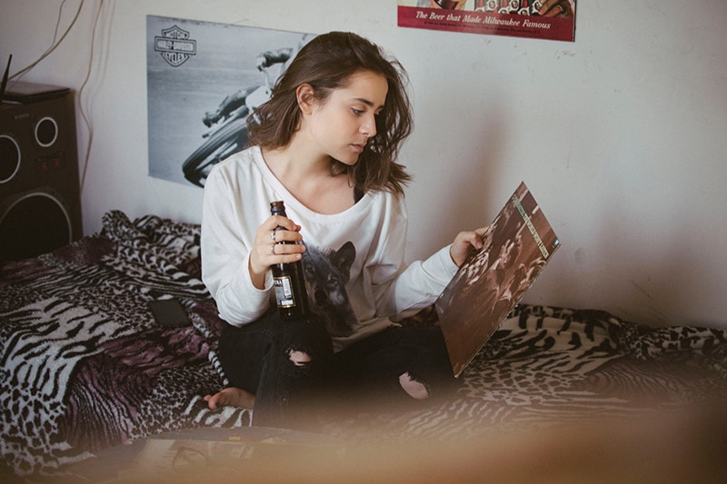 woman sitting on bed with beer in her hand while looking at picture