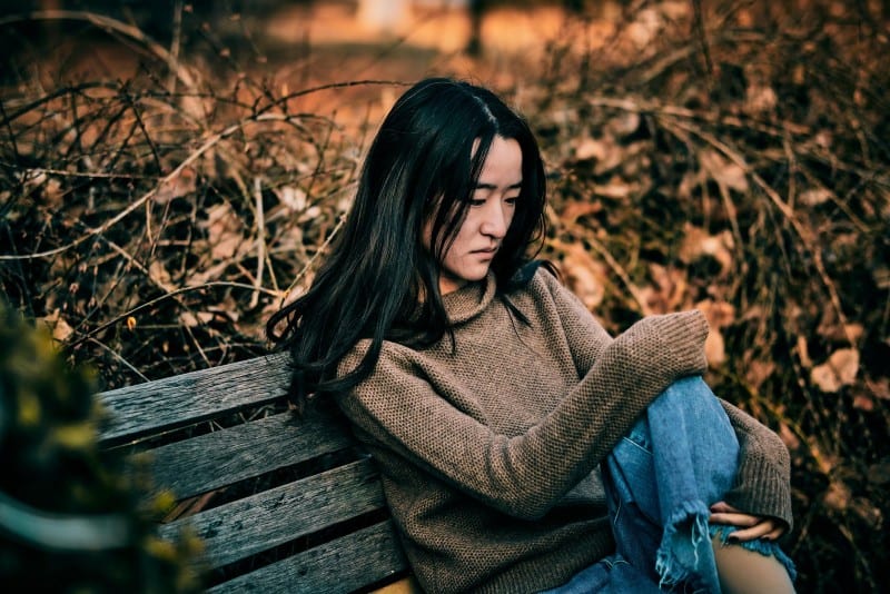 woman in grey sweater sitting on brown wooden bench
