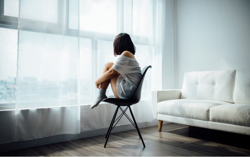 mujer sentada en una silla negra frente a una ventana de cristal con cortinas blancas