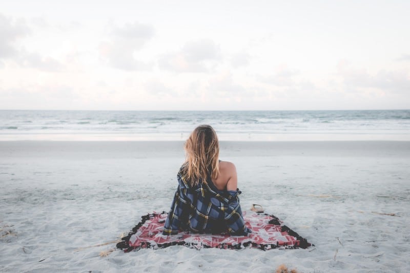 donna seduta su una coperta sulla spiaggia che guarda l'oceano