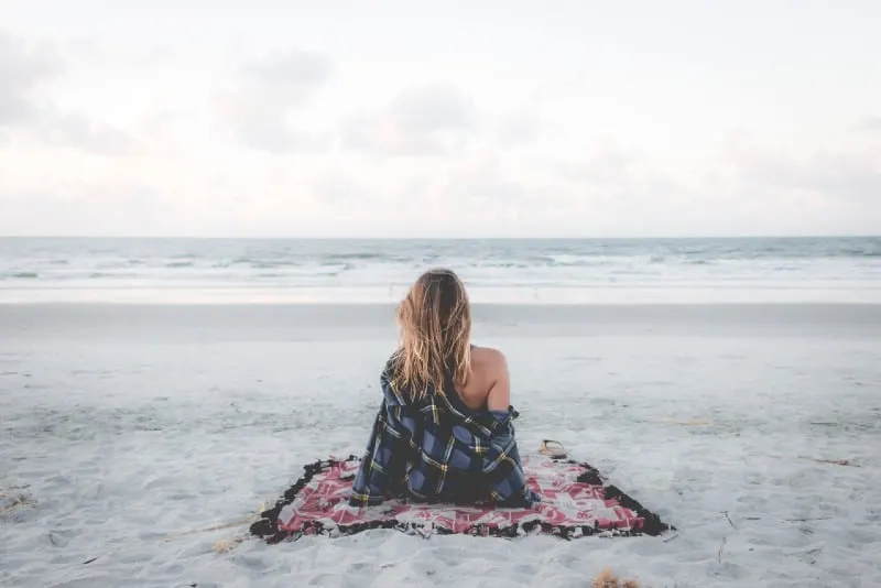 woman sitting on blanket on beach looking at ocean