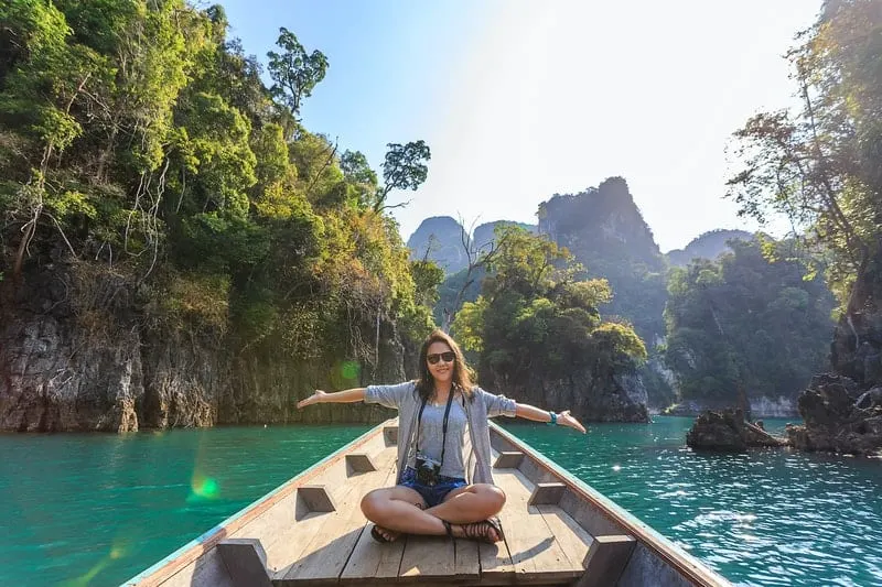 woman sitting on boat spreading her arms in the middle of a beautiful nature